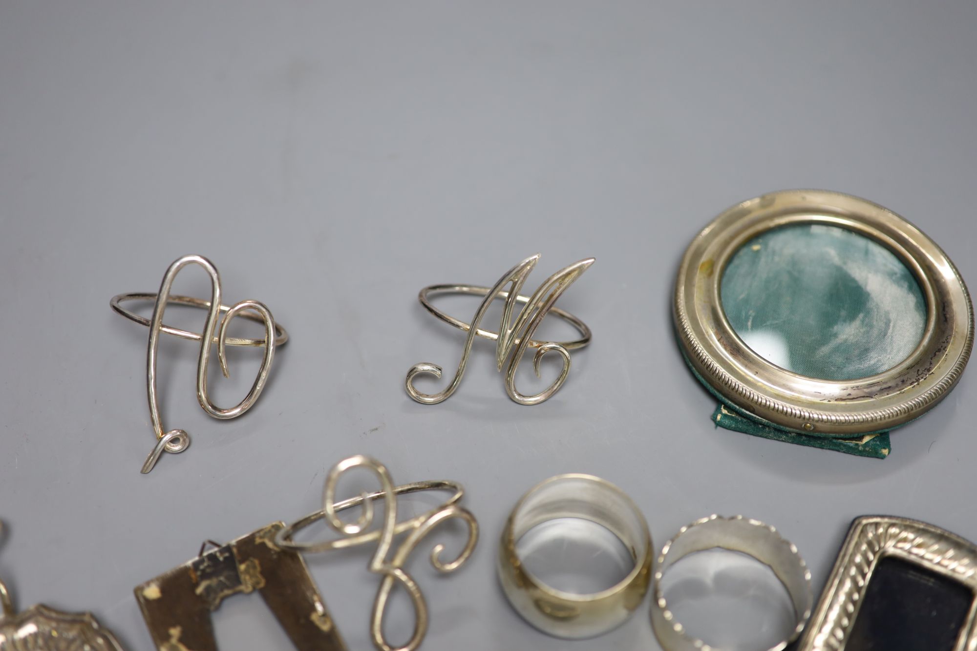 A set of four silver wire initial napkin rings, two other silver napkin rings (one Asprey) and five miniature photograph frames,